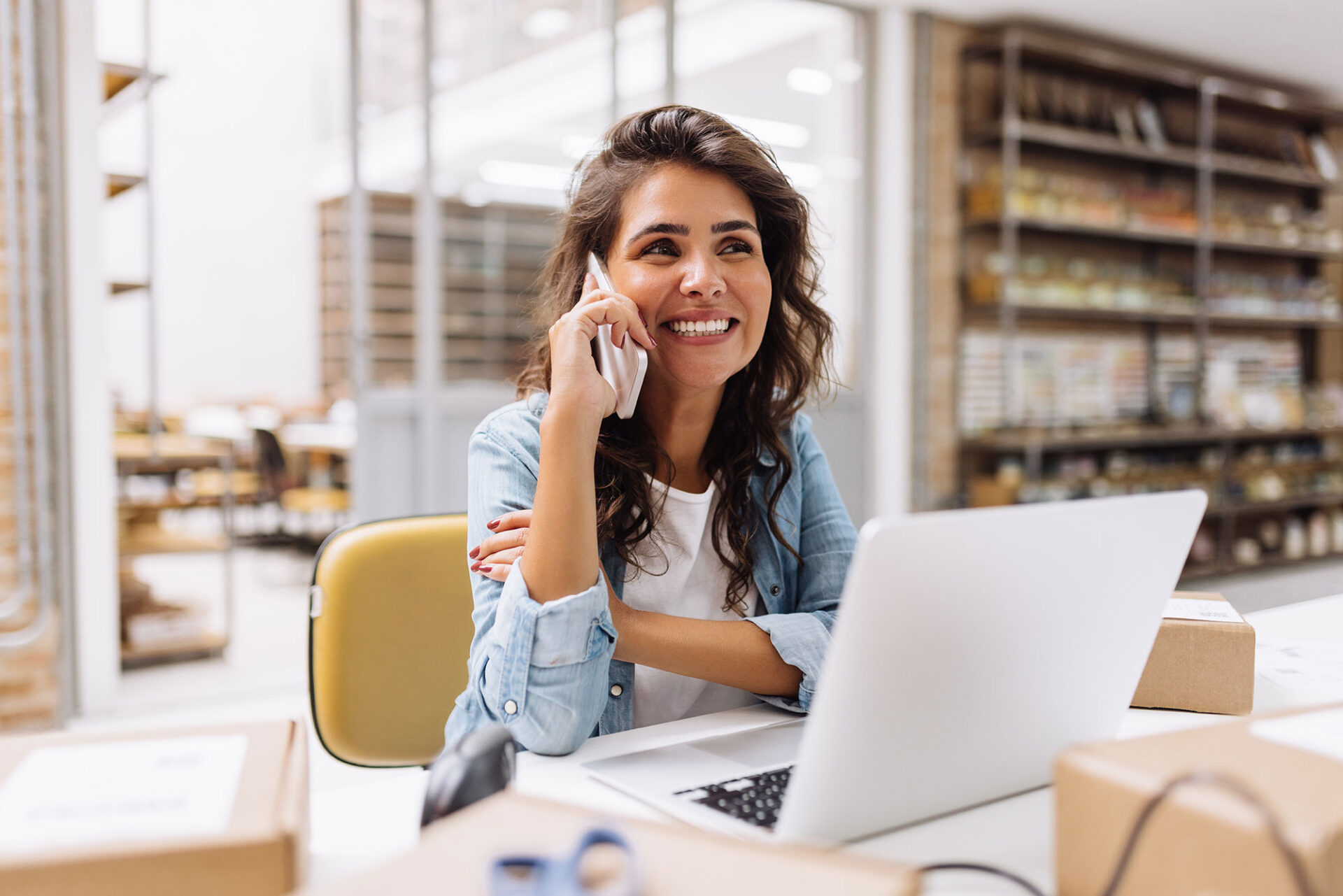 ANG | Cheerful businesswoman speaking on the phone in a warehouse