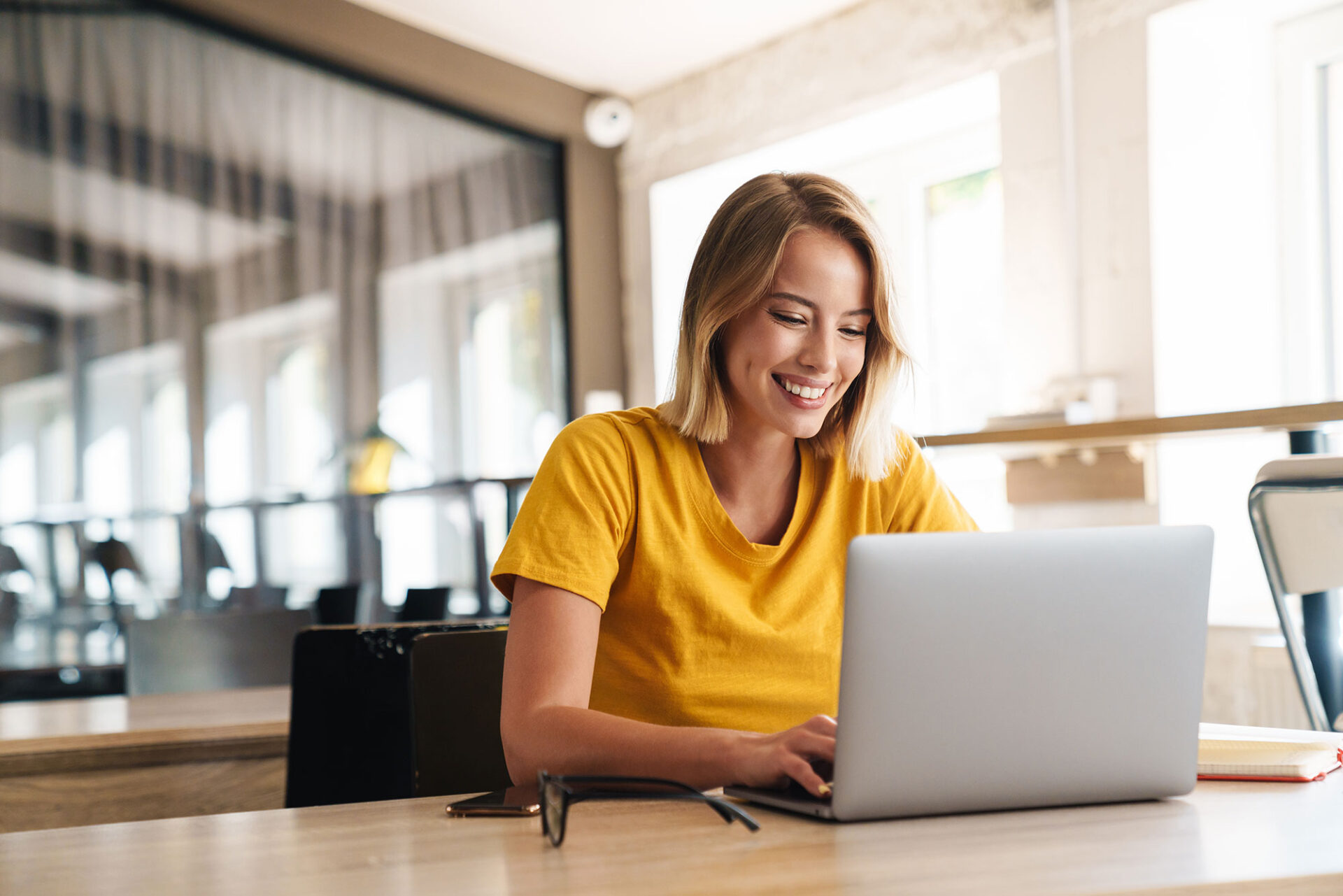 Frau blond in gelben Shirt schaut auf Laptop | ANG