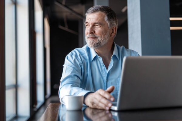 Mature businessman working on laptop. Handsome mature business leader sitting in a modern office Mature businessman working on laptop. Handsome mature business leader sitting in a modern office with large windows