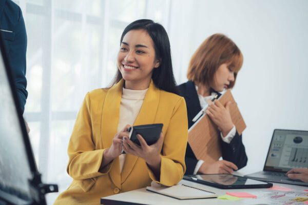 Businesswoman-in-a-yellow-blazer-smiles-confidently-as-she-takes-notes-during-a-team-meeting