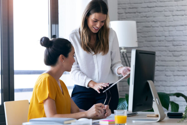 Two-young-businesswomen-reviewing-work-via-digital-tablet-in-the-office. Two-young-businesswomen-reviewing-work-via-digital-tablet-in-the-office.